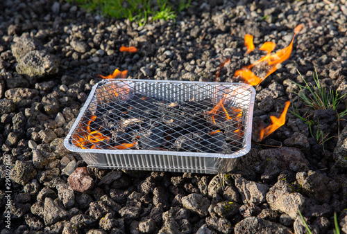 Small disposable barbecue stands on the stones. Flames come from charcoals of grill. Preparing BBQ, Iceland.