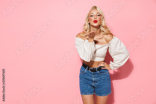 Image of glamour blonde woman with long curly hair wearing trendy clothes blowing air kiss at camera