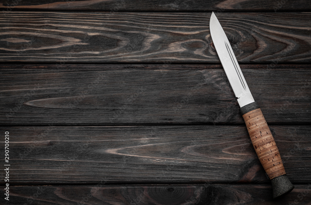 Hunting bowie knife with a wooden handle on dark wooden background. Steel arms weapon. top view Hunting bowie knife with a wooden handle on dark wooden background. Steel arms weapon. top view