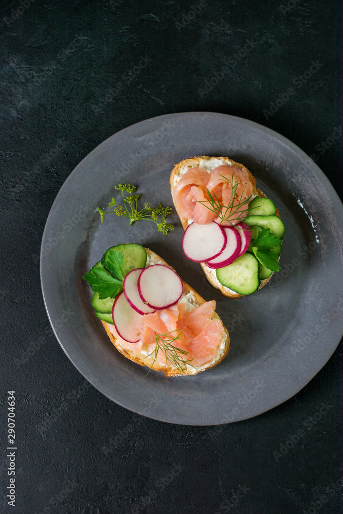 Sandwiches with smoked pink salmon, radish, cucumber and cream cheese on gray ceramic plate and textile background. Traditional Scandinavian toast. Top view.Square image Sandwiches with smoked pink salmon, radish, cucumber and cream cheese on gray ceramic plate and textile background. Traditional Scandinavian toast. Top view.Square image
