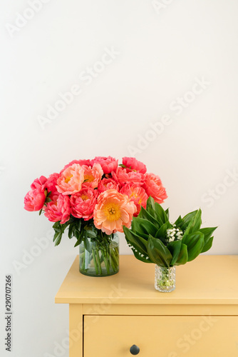 Coral peonies and spring lilies of the valley in a glass vase on wooden table.. Beautiful peony flower for catalog or online store. Floral shop concept . Beautiful fresh cut bouquet. Flowers delivery. © malkovkosta