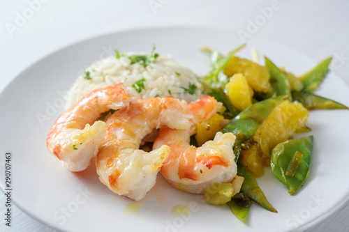 fried tiger prawn shrimps with vegetables from sugar peas and oranges, served with rice on a white plate, selected focus, narrow depth of field