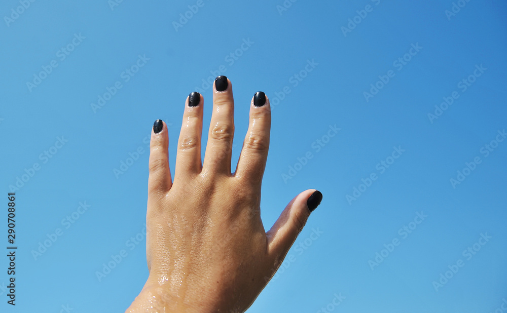 Female hand with black nails on sky background. Female hand with black nails on sky background.