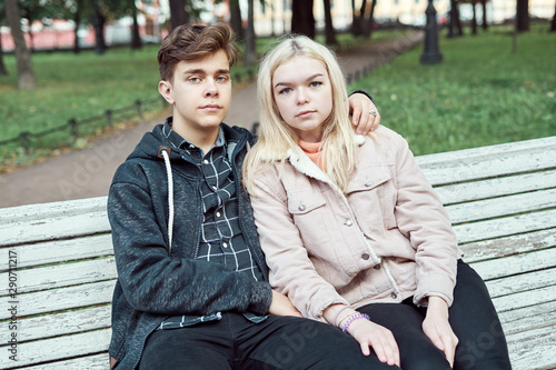 Teenagers in love sit on park bench in autumn, looking straight ahead. Concept of teen love