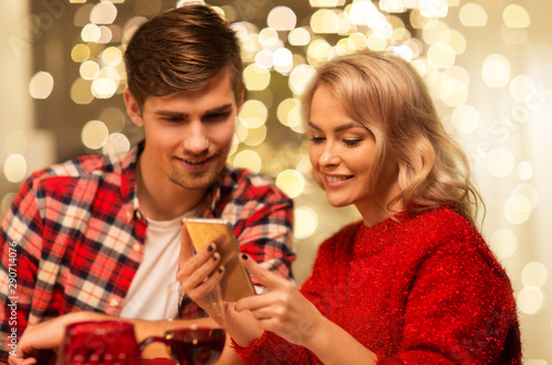holidays, technology and celebration concept - happy couple having christmas dinner at home and using smartphone