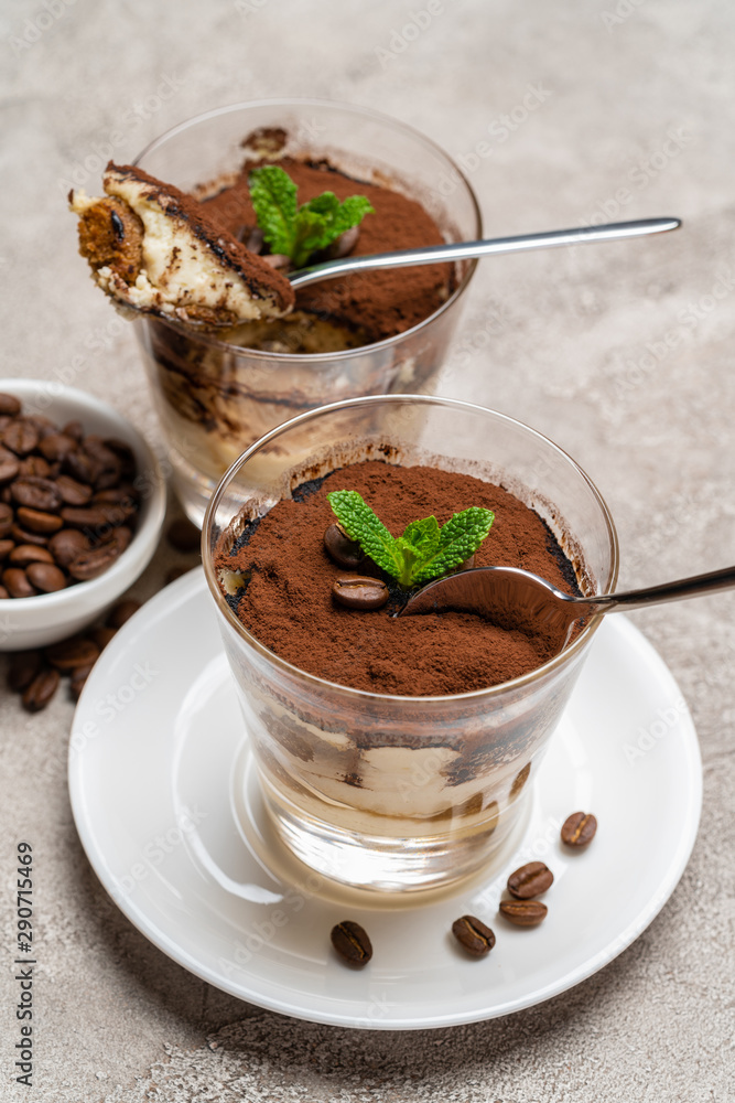 Portion of Classic tiramisu dessert in a glass cup on concrete background Portion of Classic tiramisu dessert in a glass cup on concrete background