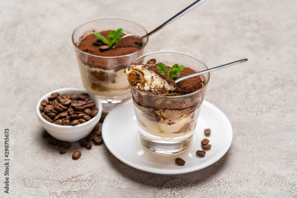 Portion of Classic tiramisu dessert in a glass cup on concrete background Portion of Classic tiramisu dessert in a glass cup on concrete background