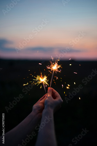 Hands holding sparkling fireworks to the sky at twilight