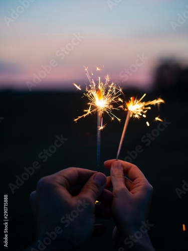 Two hands holding sparkling fireworks to the sky at twilight