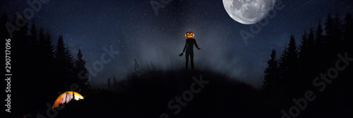 Halloween theme: scary maniac with pumpkin head in dark forest on sky background with midnight moon. People in camping don't know what the danger. Horrible fantasy. October, horror concept.