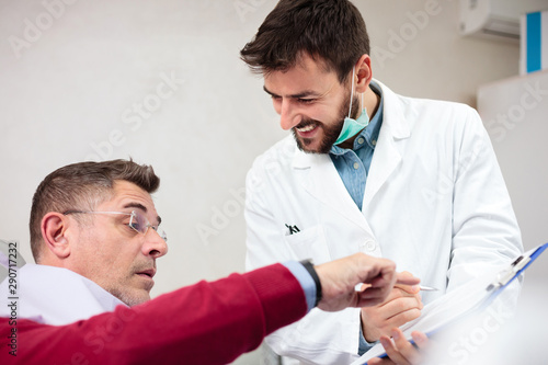 Serious mature man consulting with his doctor in medical clinic. Happy young doctor examining male patient in his office, filling out forms on a clipboard