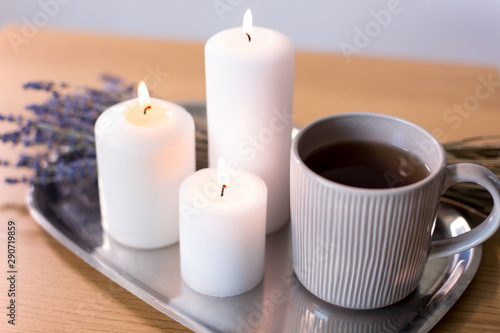decoration  hygge and cosiness concept - burning white candles  tea in mug and lavender flowers on tray on table