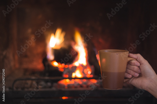 Hand holding a cup of coffee in front of the heat of a burning fireplace