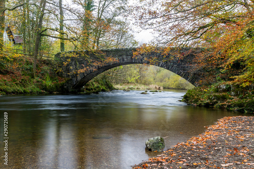 Clappersgate Bridge in the Lake District National Park at Autumn with gold & brown leaves of the ground and tree foliage turning yellow. 