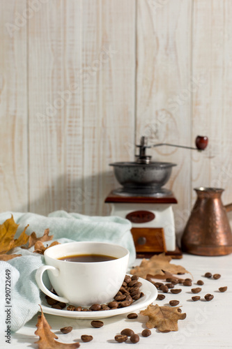 Dry yellow leaves, blue scarf, coffee grains and a cup on a white table, morning start day. Autumn mood background, copy space.