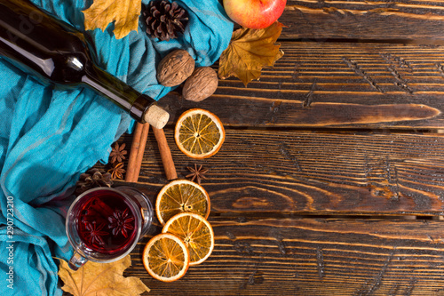 Cup of mulled wine with spices, bottle, scarf, dry leaves and oranges on a wooden table. Autumn mood, method to keep warm in the cold, copy space.