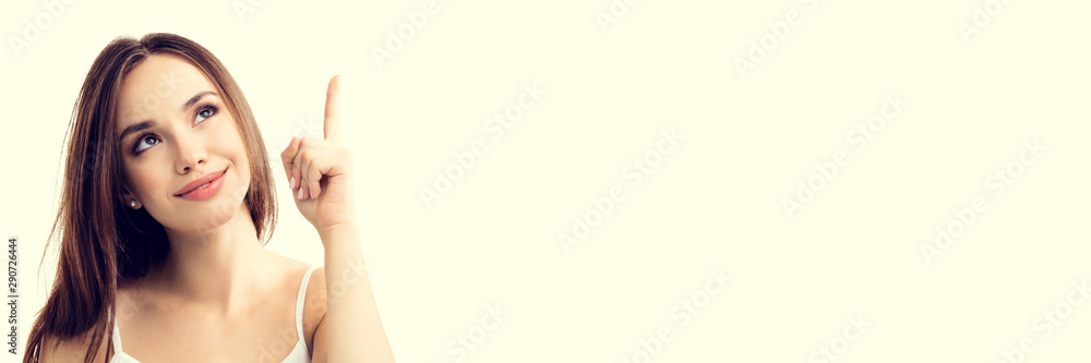 Fototapeta premium Smiling looking up young woman in casual smart clothing, showing something or copy space for text or slogan, or making idea gesture, isolated over yellow