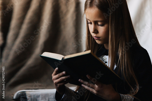 Little girl in a black dress holds a green book and reads it.