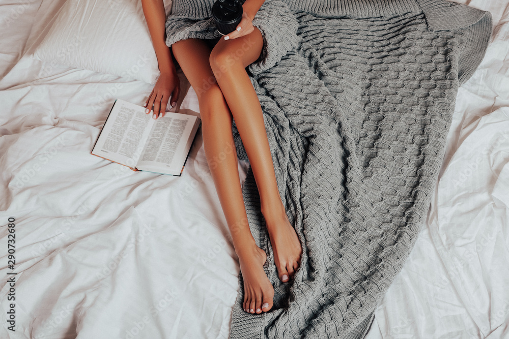 Beautiful female Legs. Winter mood, warmth and comfort. Girl Reads a Book.  Sexy smooth female legs. Open book. Relaxed Caucasian Girl is sitting on  the Bed and Reading a Book. Stock-Foto