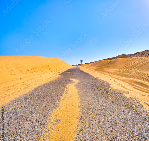 Cracked asphalt road crossing an arid dune terrain.