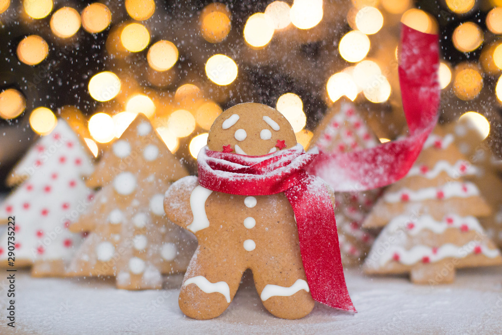 smiling gingerbread man cookie in a red scarf with christmas trees cookies and christmas lights on a background