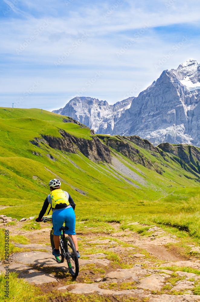 Mountain biker riding downhill in the Swiss Alps. Famous mountains Jungfrau, Eiger and Monch in the background. Mountain biking, cycling in Switzerland. Cyclist with helmet. Active lifestyle concept