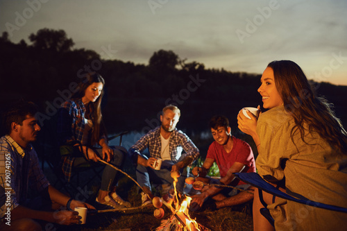 Girl with a mug of tea against the backdrop of friends by the bonfire at night