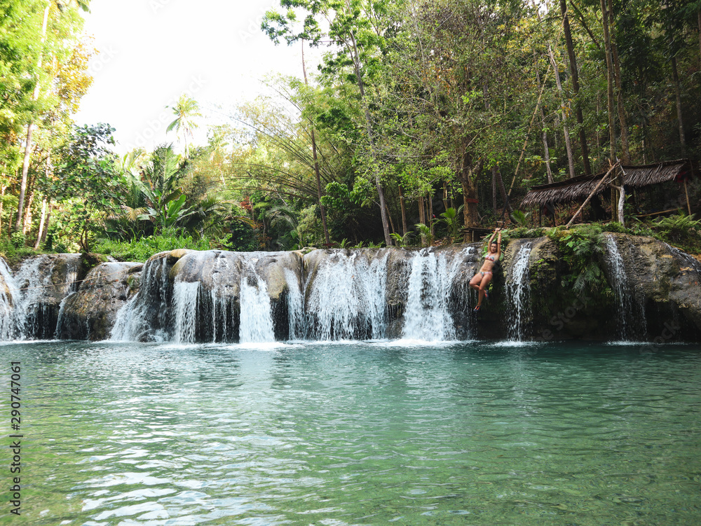 woman swinging with the rope at the pool of waterfalls, Cambugahay Falls on Siquijor Island in Philippines woman swinging with the rope at the pool of waterfalls, Cambugahay Falls on Siquijor Island in Philippines