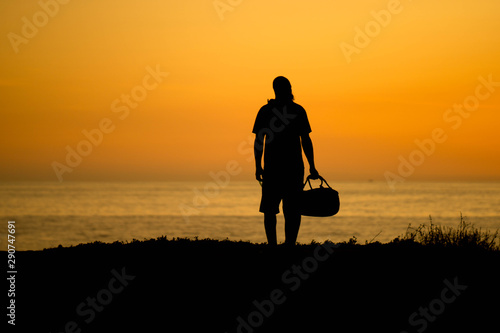 silhouette of a man wearing a beanie and holding a duffle bag summer travel concept