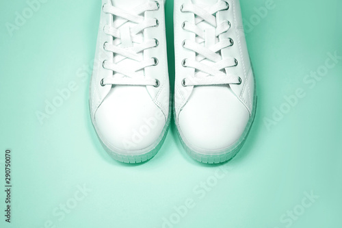 White sneakers are lying on mint color background.