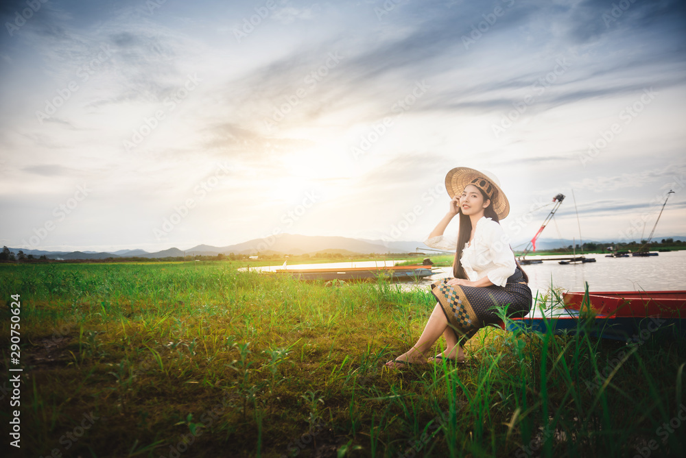 Asian Beautiful woman in Thai local dress sitting on boat in fishing village with field and lake background Asian Beautiful woman in Thai local dress sitting on boat in fishing village with field and lake background