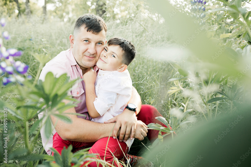 a father hugs with his son and they sit among greenery lawn