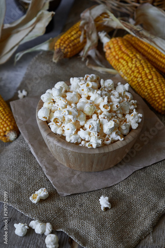 Traditional popcorn in a wooden bowl and corncobs on the table.