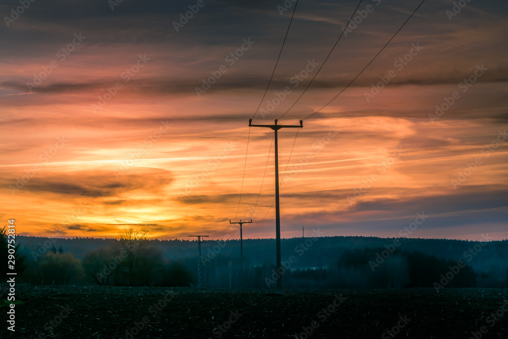 Colorful orange sunset over rolling rural hills with silhouetted poles in a scenic landscape in a weather concept