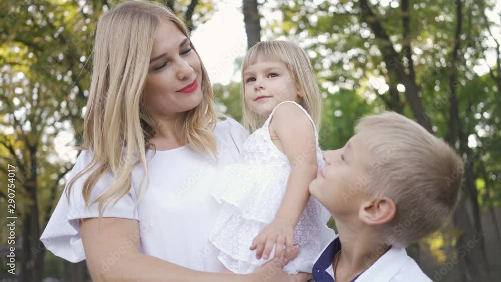 Young blond woman holding baby daughter in her arms while older son standing next to them. Happy family with two kids. Leisure activity, connecting with nature. Young blond woman holding baby daughter in her arms while older son standing next to them. Happy family with two kids. Leisure activity, connecting with nature.