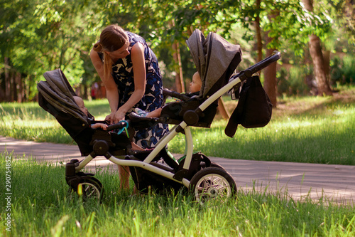 Woman and stroller for twins. A beautiful woman in a park seats two children up to a year in a stroller for twins. Maternity, Modern solutions for twins.