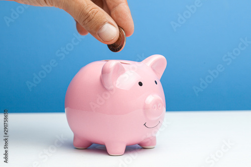 Pink piggy bank and coin in a male hand on a blue background