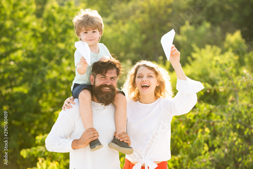 Family holiday and togetherness. Spring time. Happy child showing his parents paper airplane. Portrait of happy father giving son piggyback ride on his shoulders and looking up.