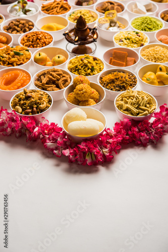 Rangoli of sweets and Farsan/snacks in bowls for Diwali with diya over white background