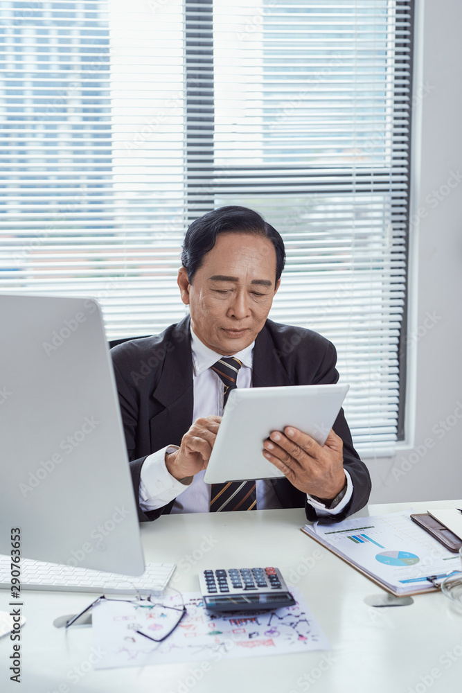 Smiling asian businessman using tablet in office Smiling asian businessman using tablet in office
