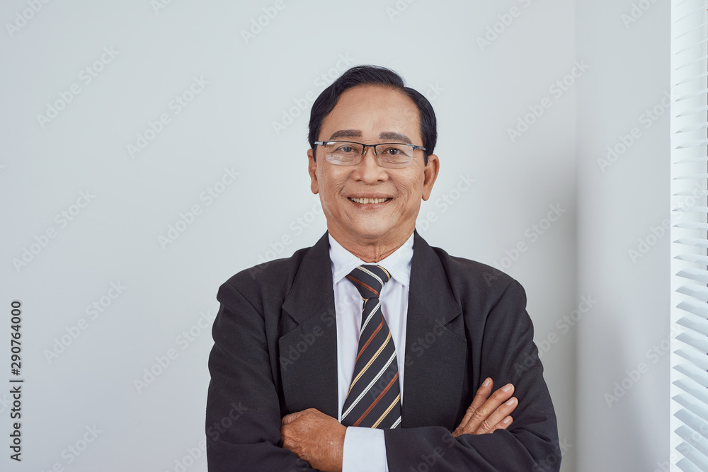 Smiling attractive mature man wearing glasses leaning on the sill of a large bright window with copy space looking at the camera Smiling attractive mature man wearing glasses leaning on the sill of a large bright window with copy space looking at the camera