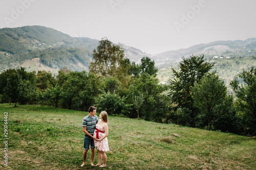 In waiting baby. happy family. pregnant woman with beloved husband stand, holds hand round belly barefoot on the grass. The sincere tender moments. background, mountains, forests, nature, nine month