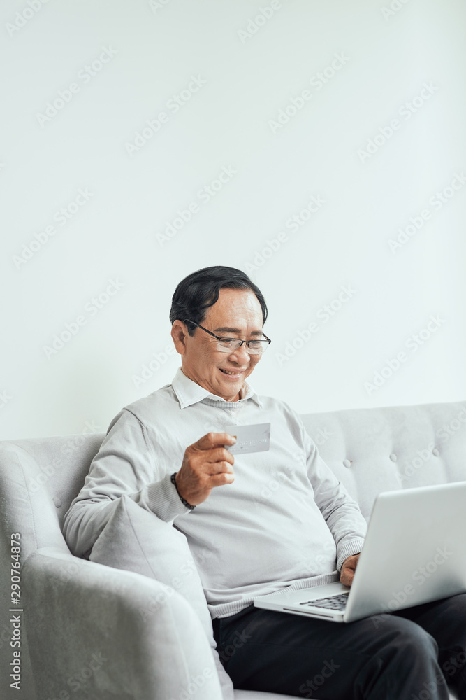 Senior man sitting in sofa and shopping online using laptop Senior man sitting in sofa and shopping online using laptop