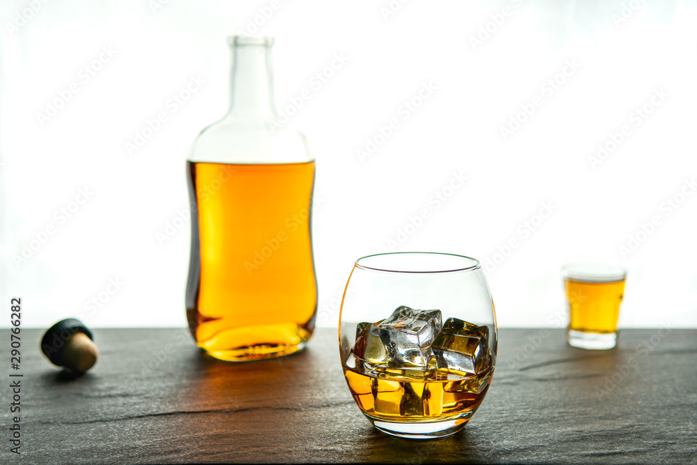 A simple and elegant whiskey (whisky) bottle, shot and glass with ice on a dark stone base with a white background with copy space A simple and elegant whiskey (whisky) bottle, shot and glass with ice on a dark stone base with a white background with copy space