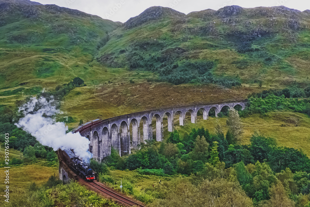 Historical steam train passing stone viaduct.