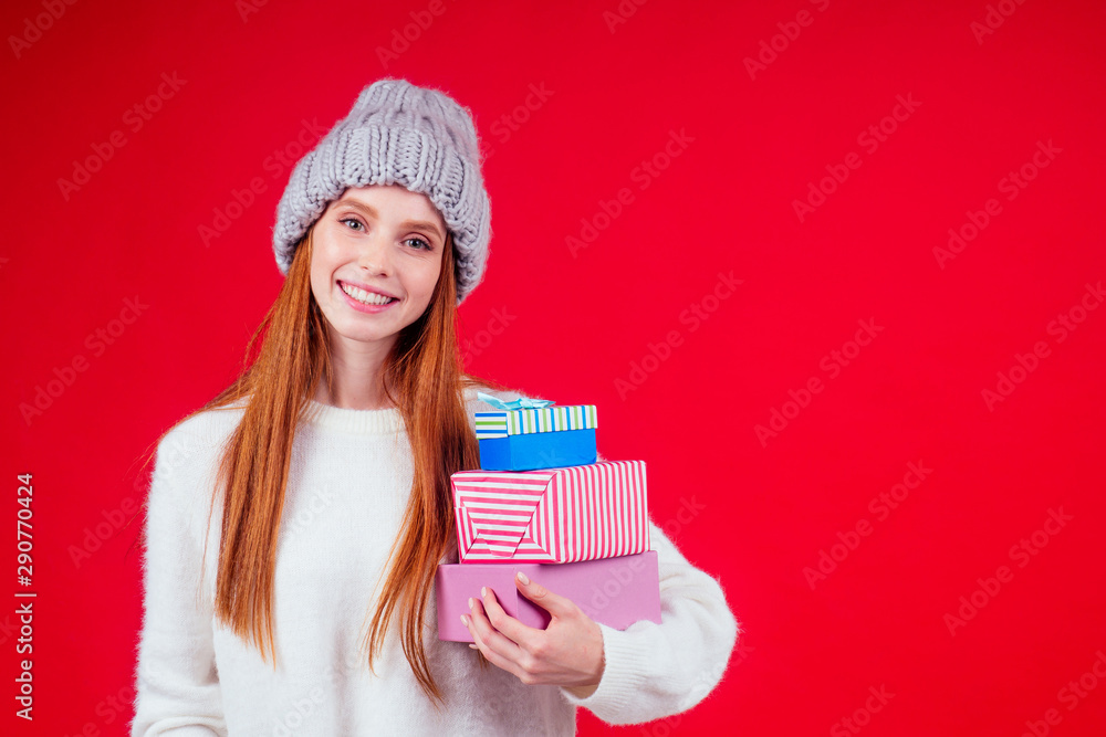 redhaired ginger woman wear stylish wool hat and white sweater looking at camera and holding three boxes witg gifts copyspase in studio red background redhaired ginger woman wear stylish wool hat and white sweater looking at camera and holding three boxes witg gifts copyspase in studio red background