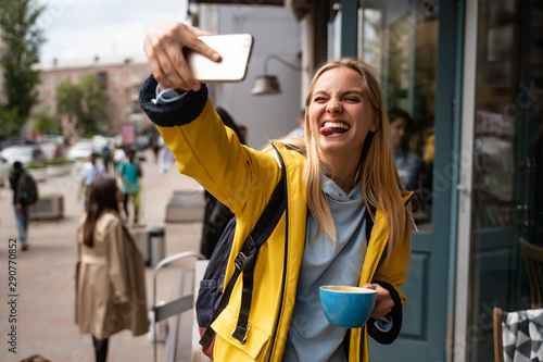 Enchanting blonde young woman with smartphone take selfie on the street