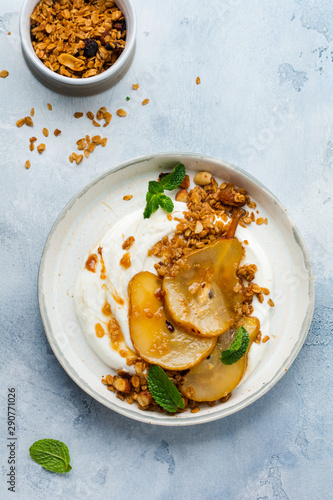 Greek yogurt with caramelized pear, granola, nuts and melted sugar for a wholesome breakfast on a gray ceramic plate. Rustic style. Top view.
