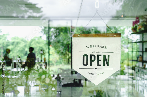 Welcome and open sign hanging on window glass in coffee shop.