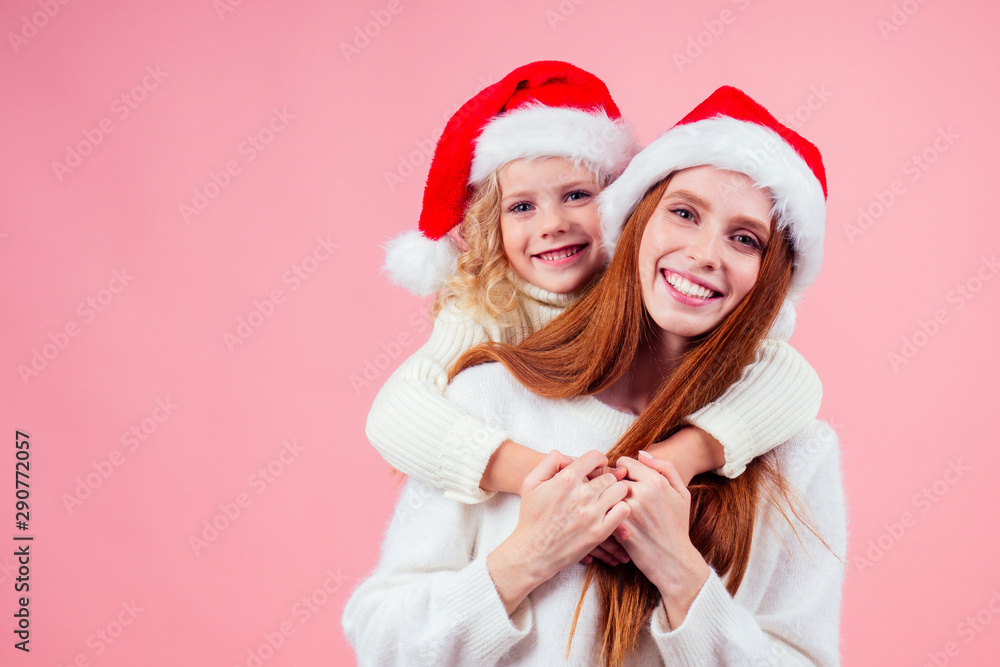 ,happy redhead ginger woman and cute little blonde girl wearing santa claus hat and having fun together in studio pink background ,happy redhead ginger woman and cute little blonde girl wearing santa claus hat and having fun together in studio pink background